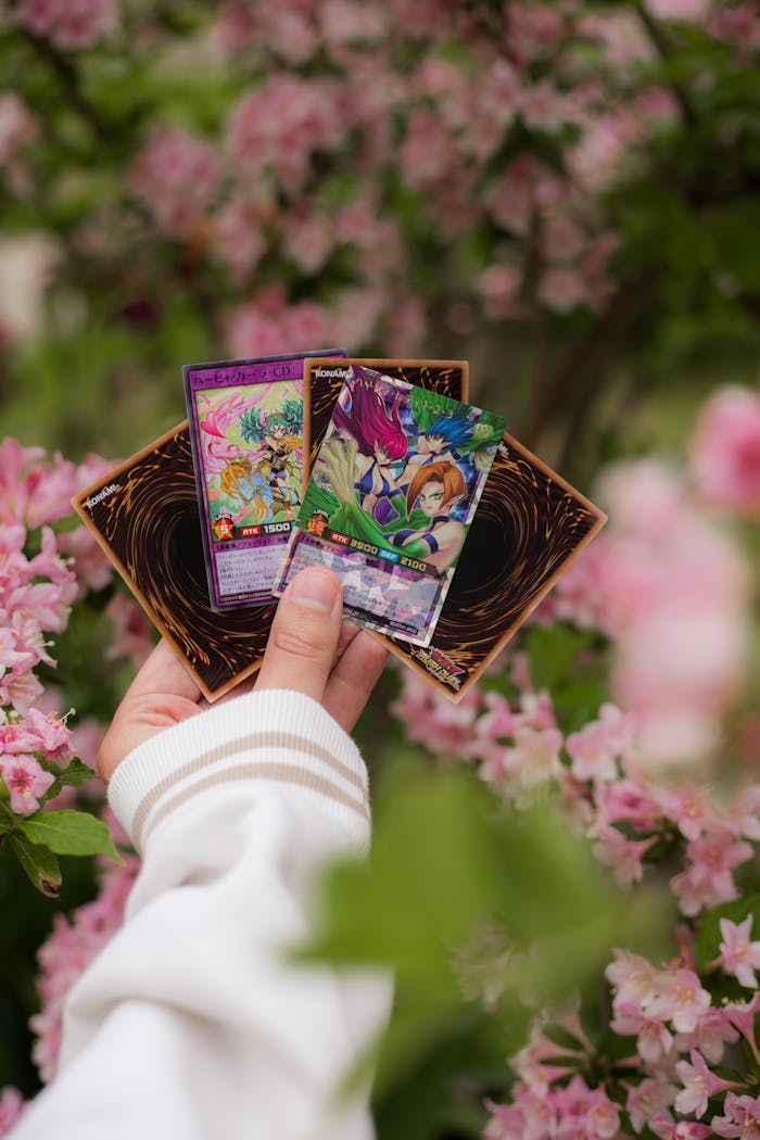 A hand holding Yu-Gi-Oh! cards with vibrant floral background, perfect for collectors and enthusiasts.